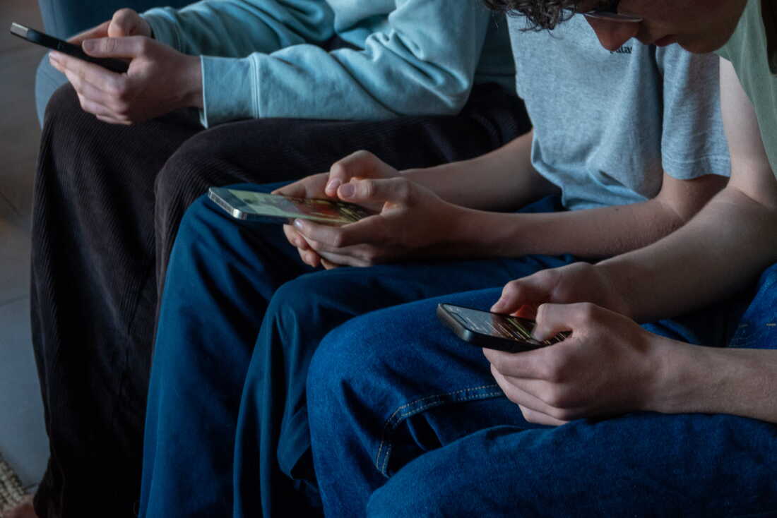 Three teen boys intently use their smartphones. They are sitting next to one another and are looking down at their phones.