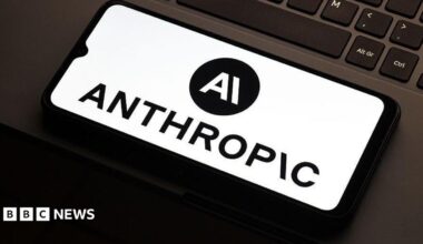 Anthropic logo on a smarthphone which is lying flat on the mousepad of a laptop. Only a partial keyboard of the laptop is visible.