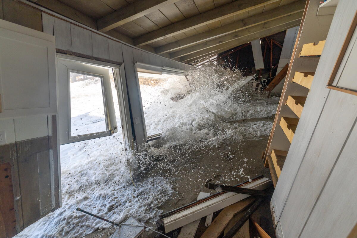 A wave driven by high tide and high surf crashes through an oceanfront home.