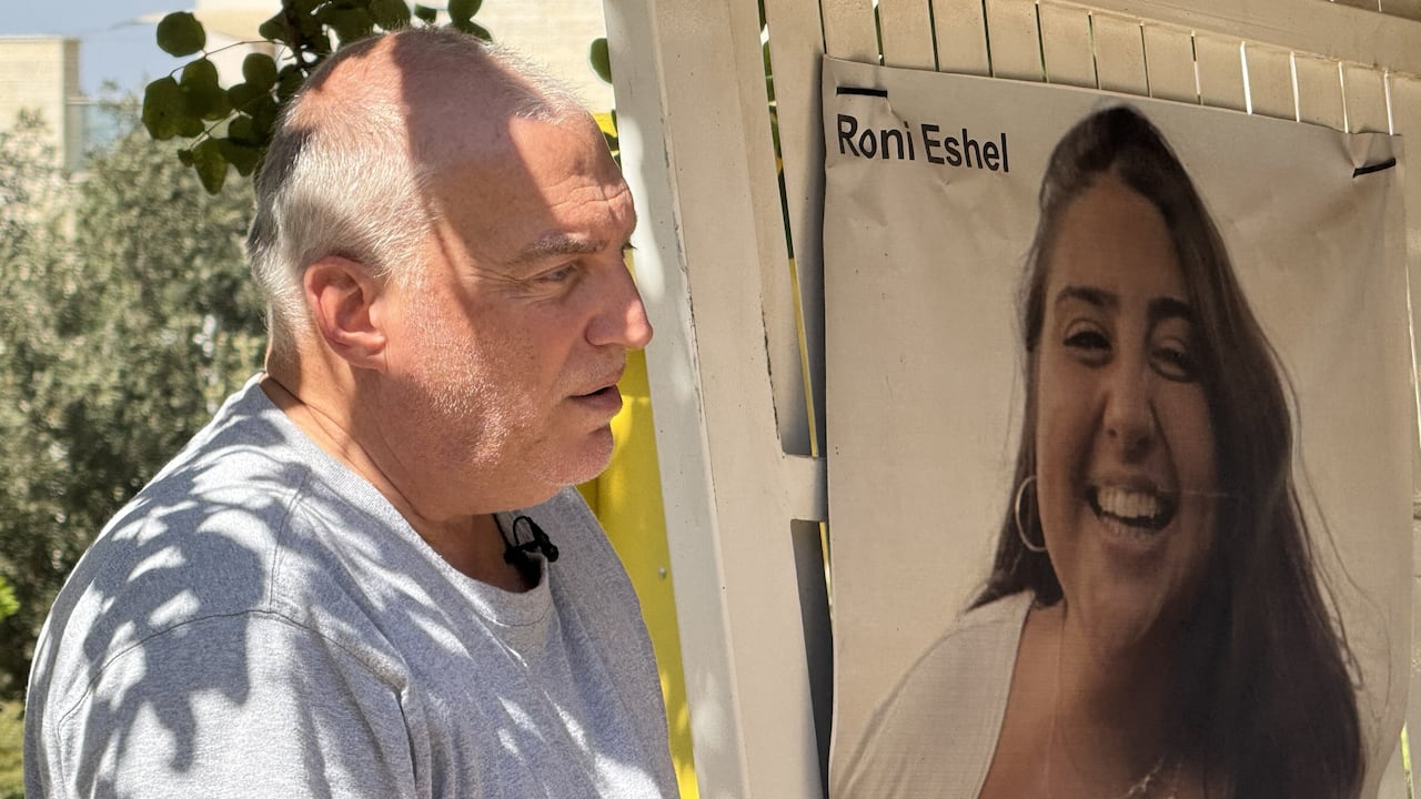 A man standing outdoors looks at a poster of a smiling young woman