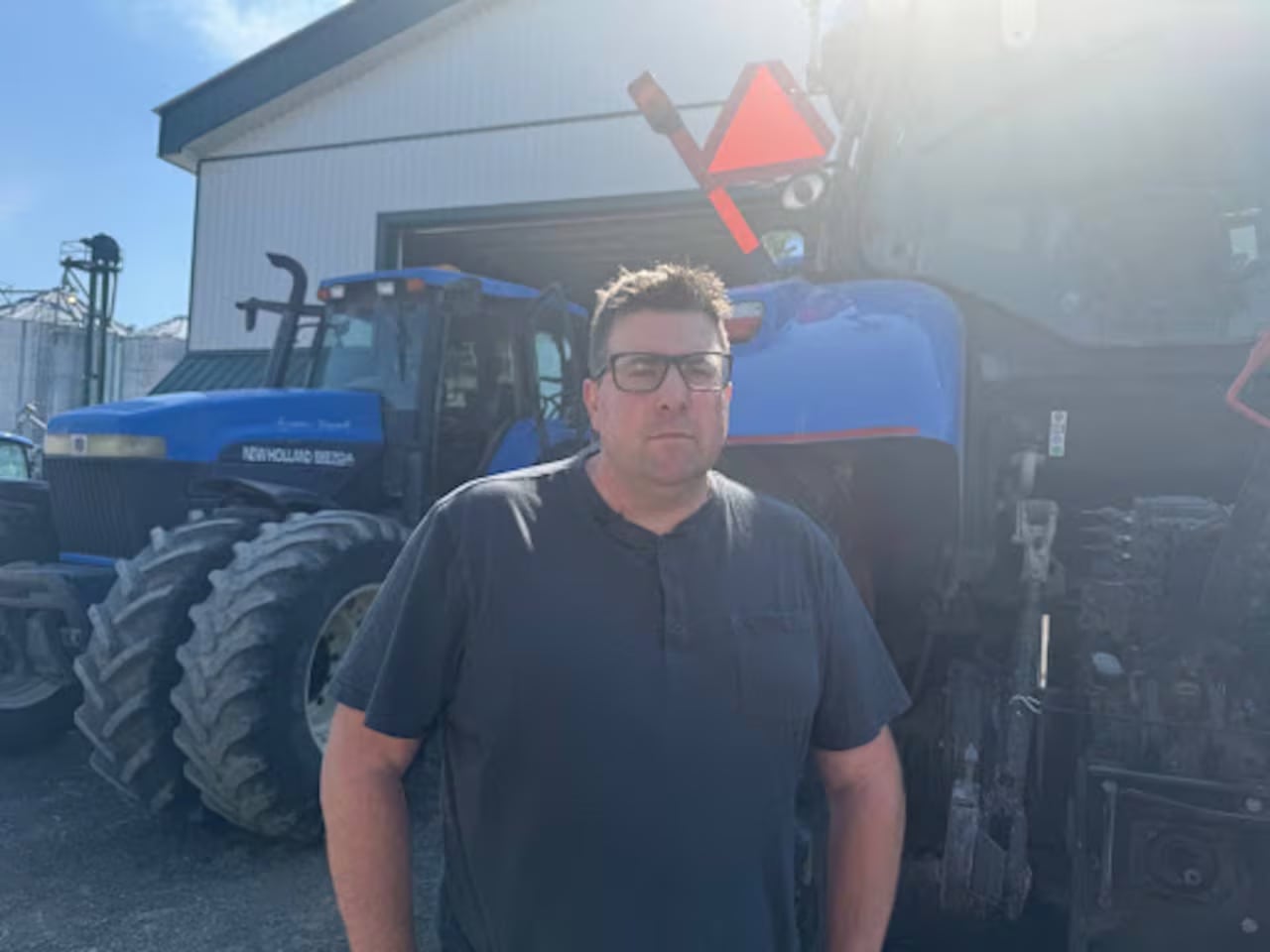 Man in dark blue shirt stands outside a tractor