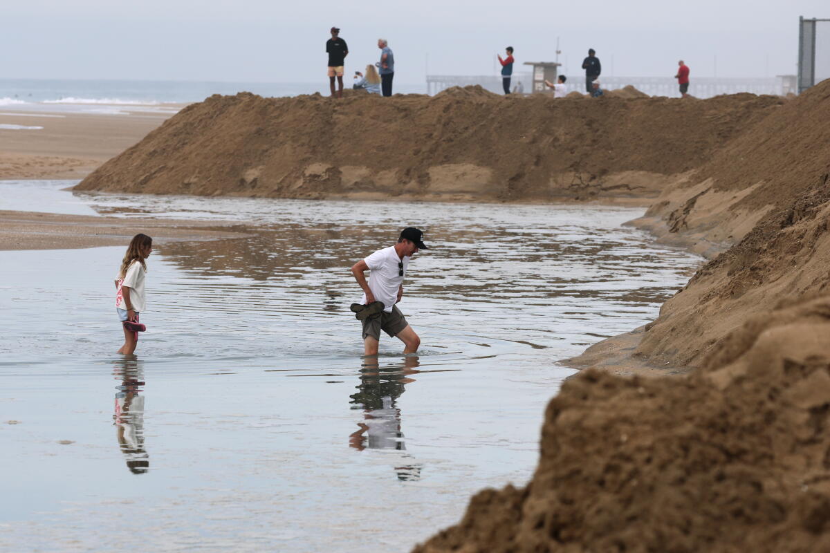 Mike Carter and his daughter Ellie Carter, 11, wade through ocean water that washed over the beach in Newport Beach.