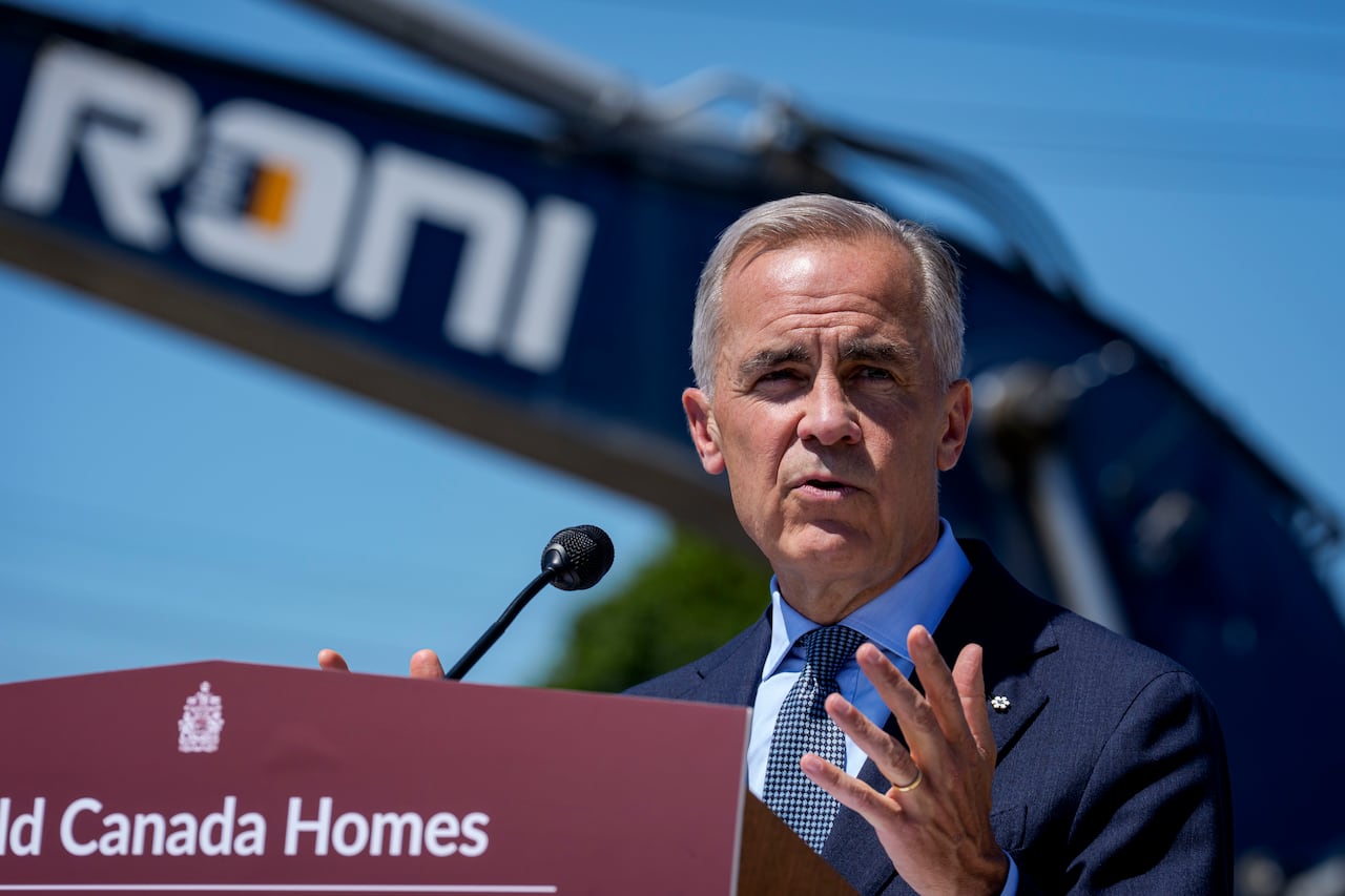 Prime Minister Mark Carney in front of a Build Canada Homes podium and construction equipment.