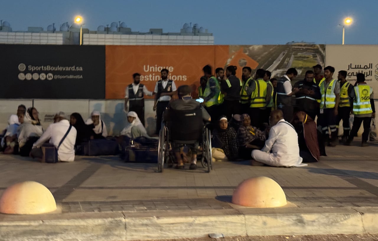 People gather on a sidewalk, some wearing high-viz vests.