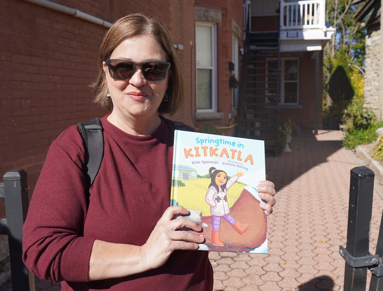 A woman holding a book up smiles at the camera.