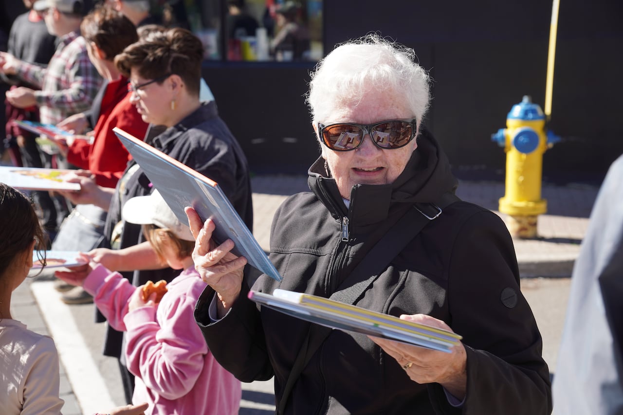 A photo of a line of people handing books down the line to each other. The focus is on a woman with grey hair and sun glasses holding two books.