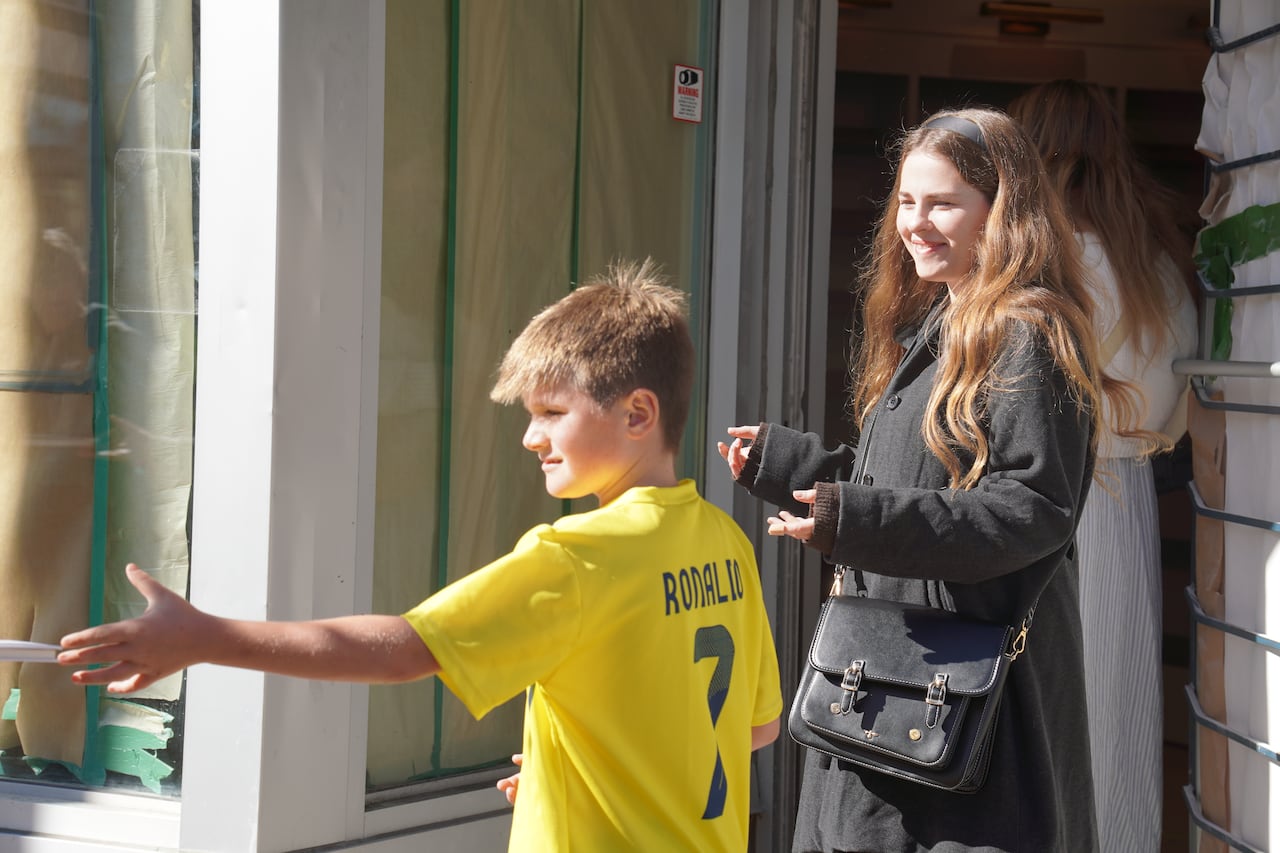 Two people wait near a store's entrance on a sunny day with their hands outstretched.