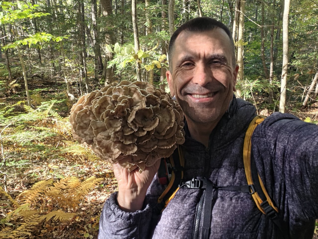 A smiling man holds a large mushroom next to his face