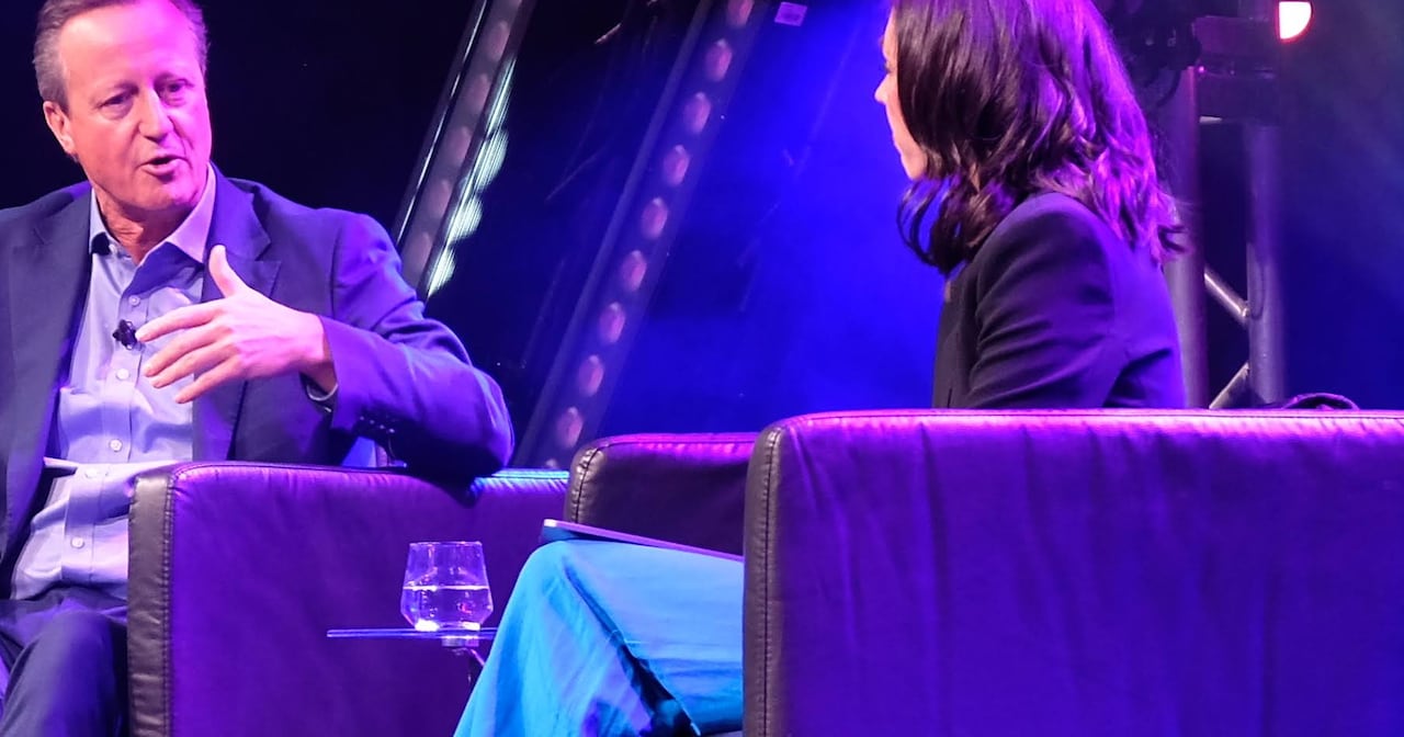 A man sitting in a chair talking to a woman on a stage under blue lights