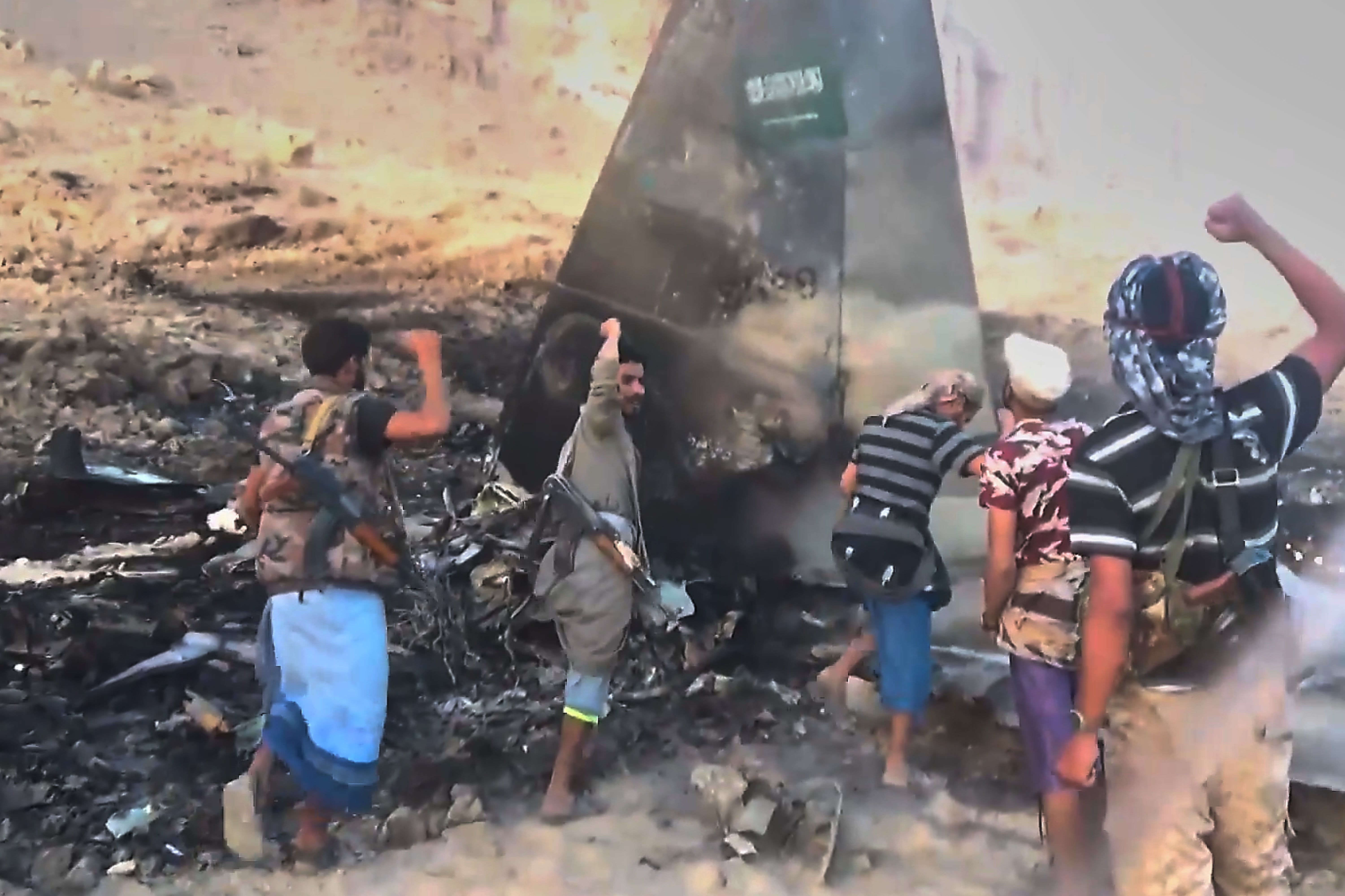Houthi fighters chant and raise their fists beside what the group described as the wreckage of a downed Saudi F-15 fighter jet