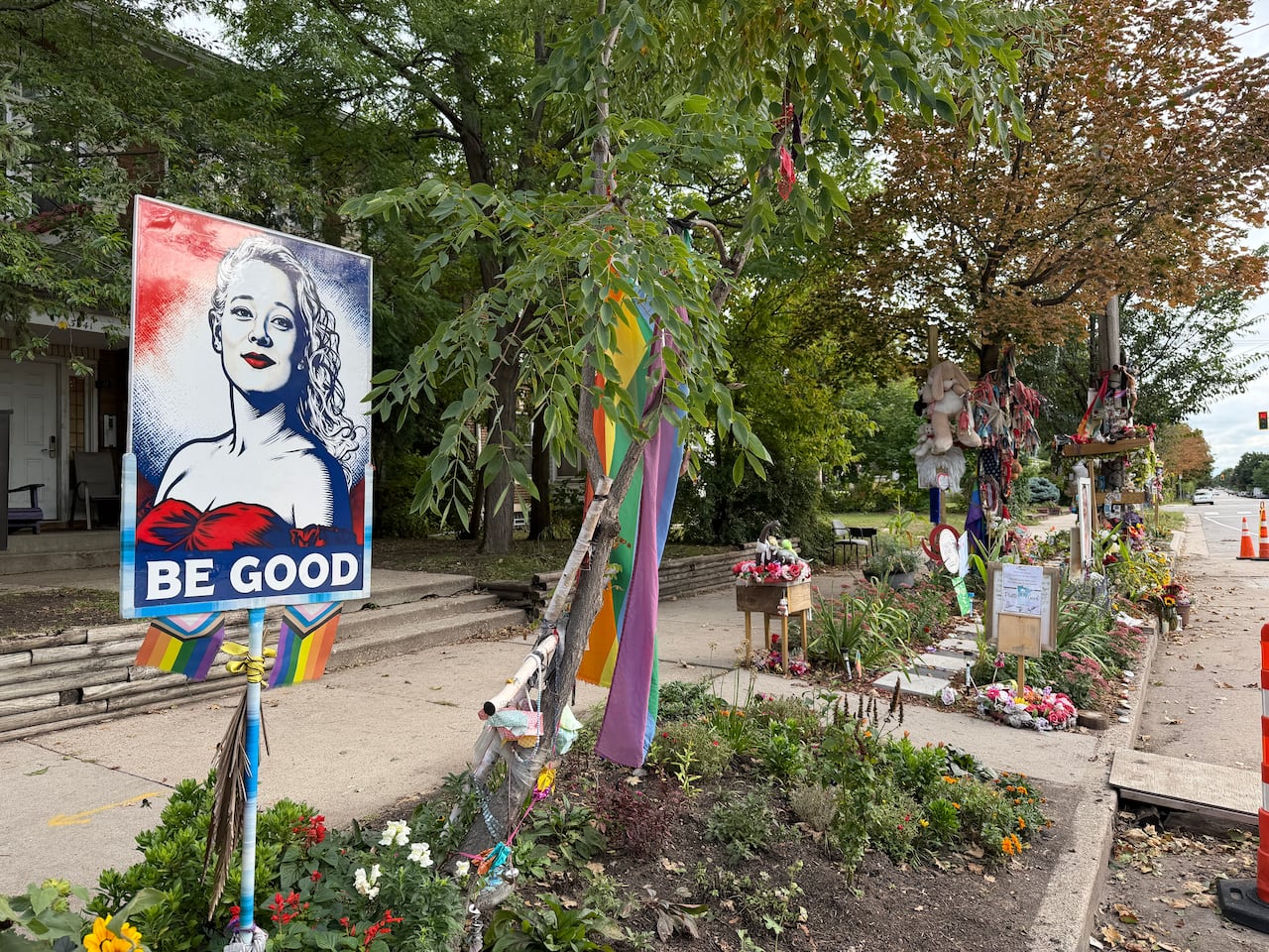 A poster showing Renee Good is festooned with Pride flags and ribbons in a garden.