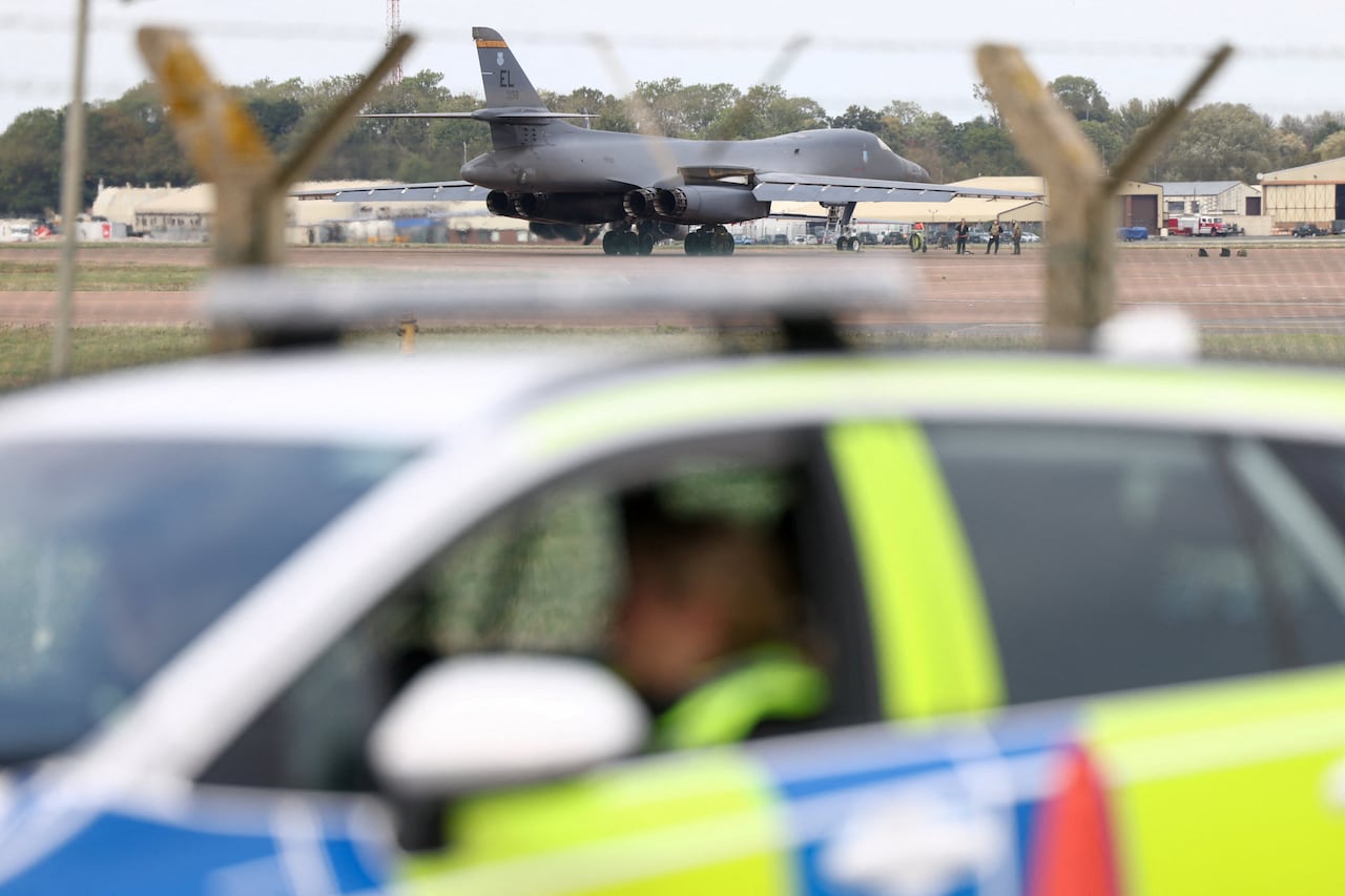 A British police car is seen in front of a grey military plane on a runway.
