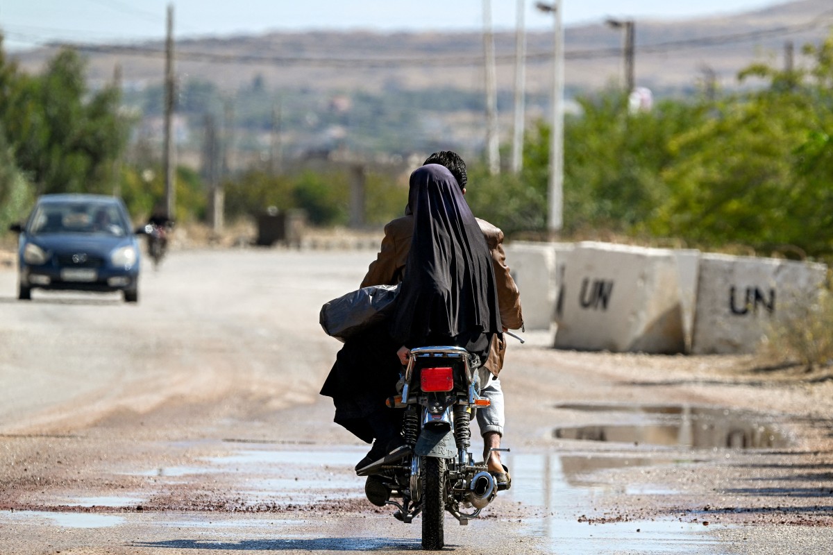 A woman rides behind a man on a motorcycle past a United Nations Disengagement Observer Force facility near Khan Arnaba in Quneitra in southwestern Syria near the Israeli-annexed Golan Heights on Oct. 7, 2026. (Photo by LOUAI BESHARA / AFP)