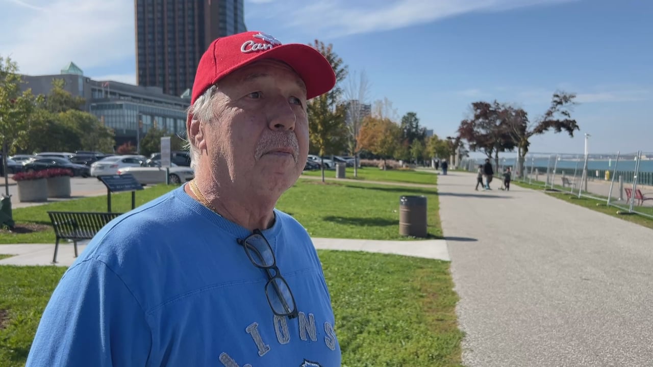A man wears a red Canada hat next to the Detroit River.