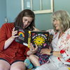 Stacia Bourne; her mother, Mary Jo Galusha; and Bourne's child are sitting on a sofa at Galusha’s home in Newark, Delaware. The child is sitting between the two women, and Bourne is holding up a children's book as the three enjoy it together.