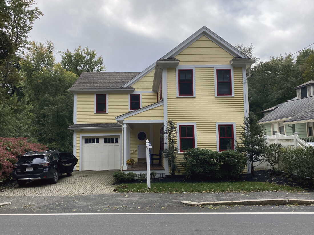 A multistory yellow house with a garage and a driveway.