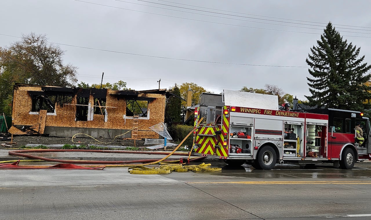 A fire truck is parked in front of a building that has burned. The building was under construction and is surrounded by fencing.