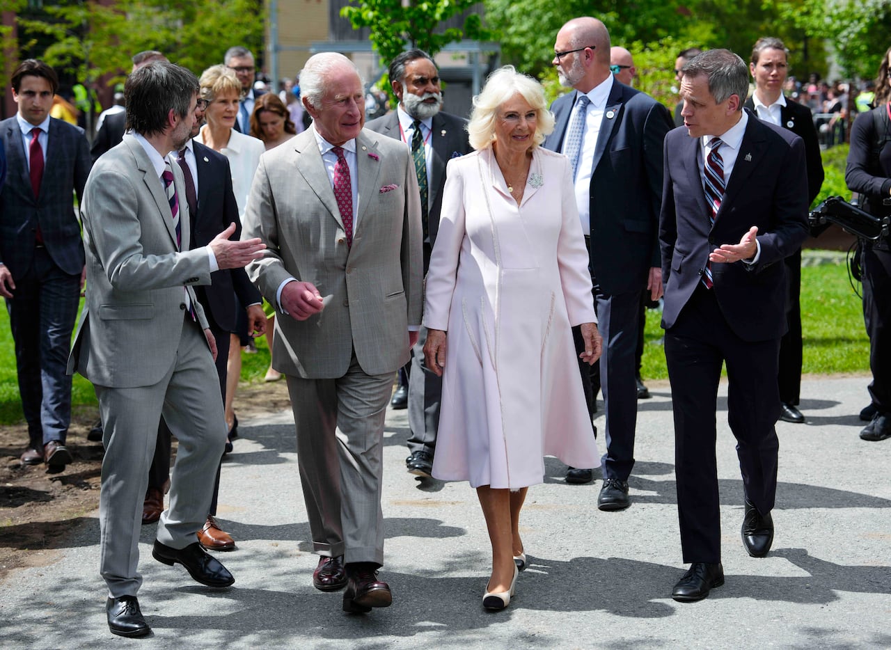 Two men walk alongside King Charles and Queen Camilla, with one gesturing at the path in front
