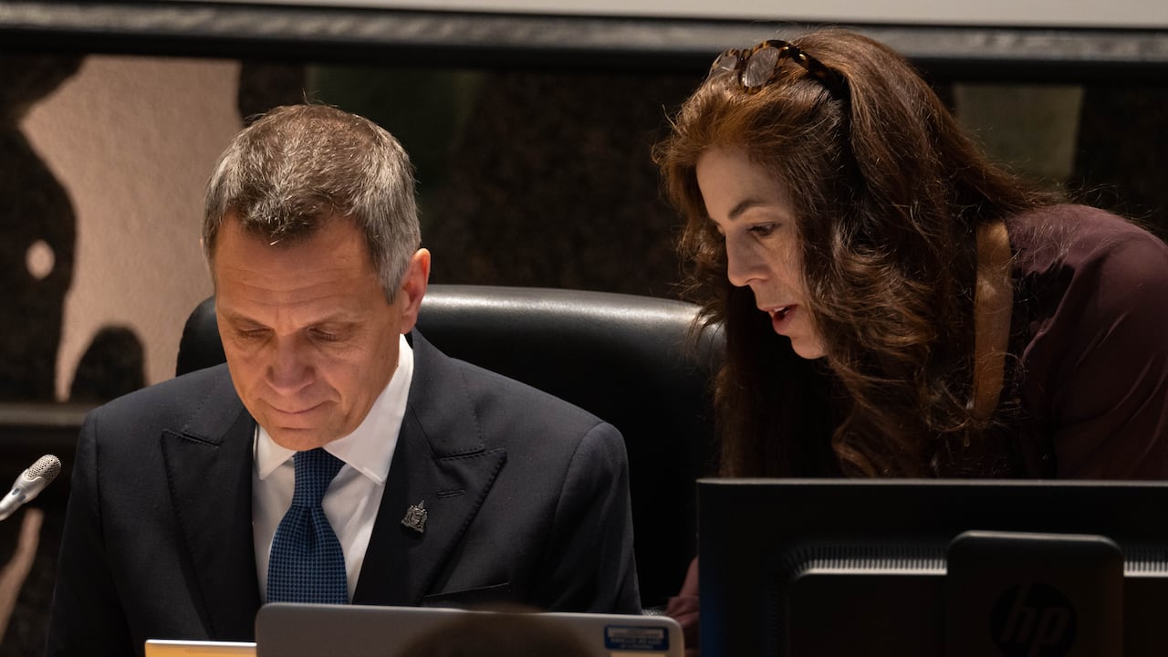 A man with grey hair looks at down at something while a woman with long hair looks at him
