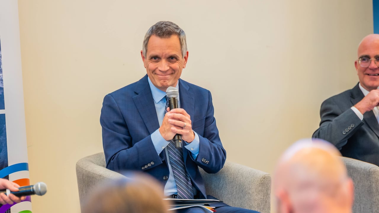 A man in a suit holds a microphone with both hands and smiles