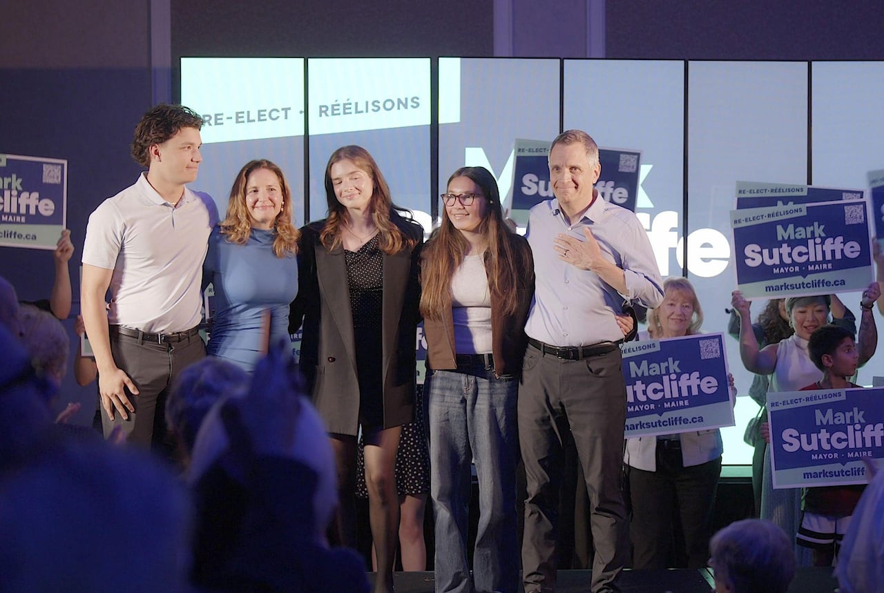 A family of five stands on a stage surrounded by people holding up campaign signs