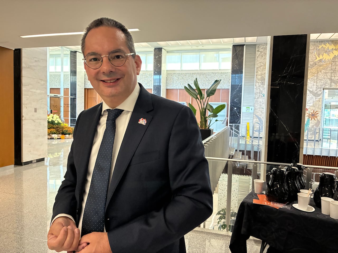 A man in a dark coloured suit stands and smiles at the camera.