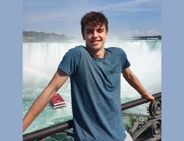 A young man smiles standing in front of a waterfall.