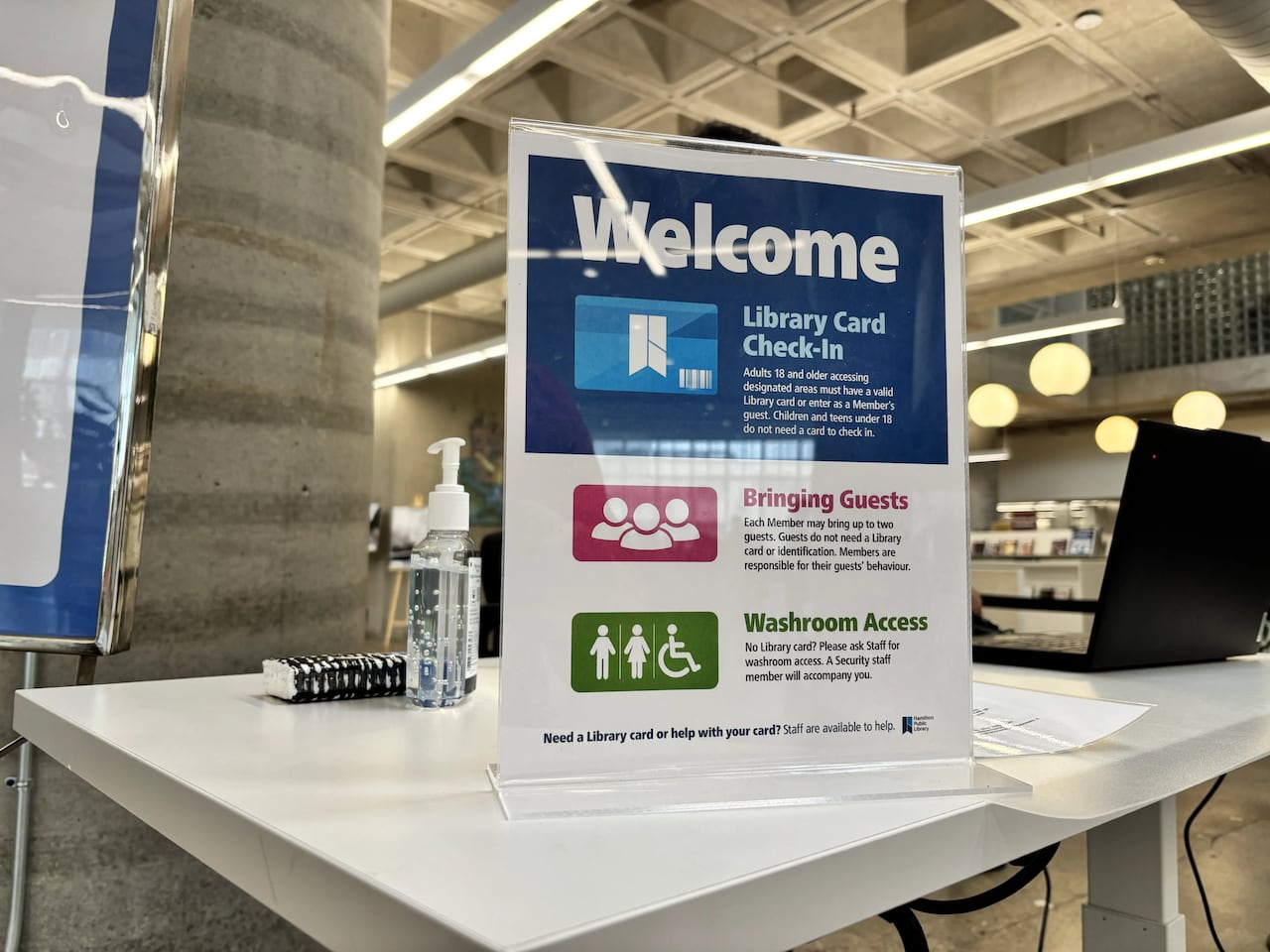 A sign sits on a desk in a library lobby.