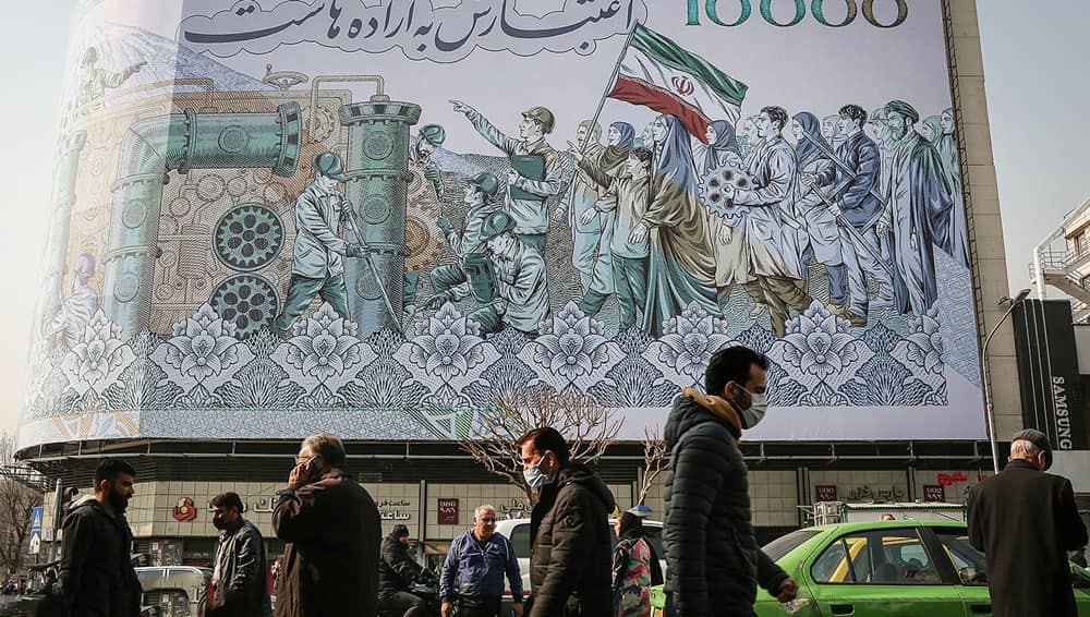 Pedestrians pass a giant banknote-style billboard showcasing state propaganda in central Tehran