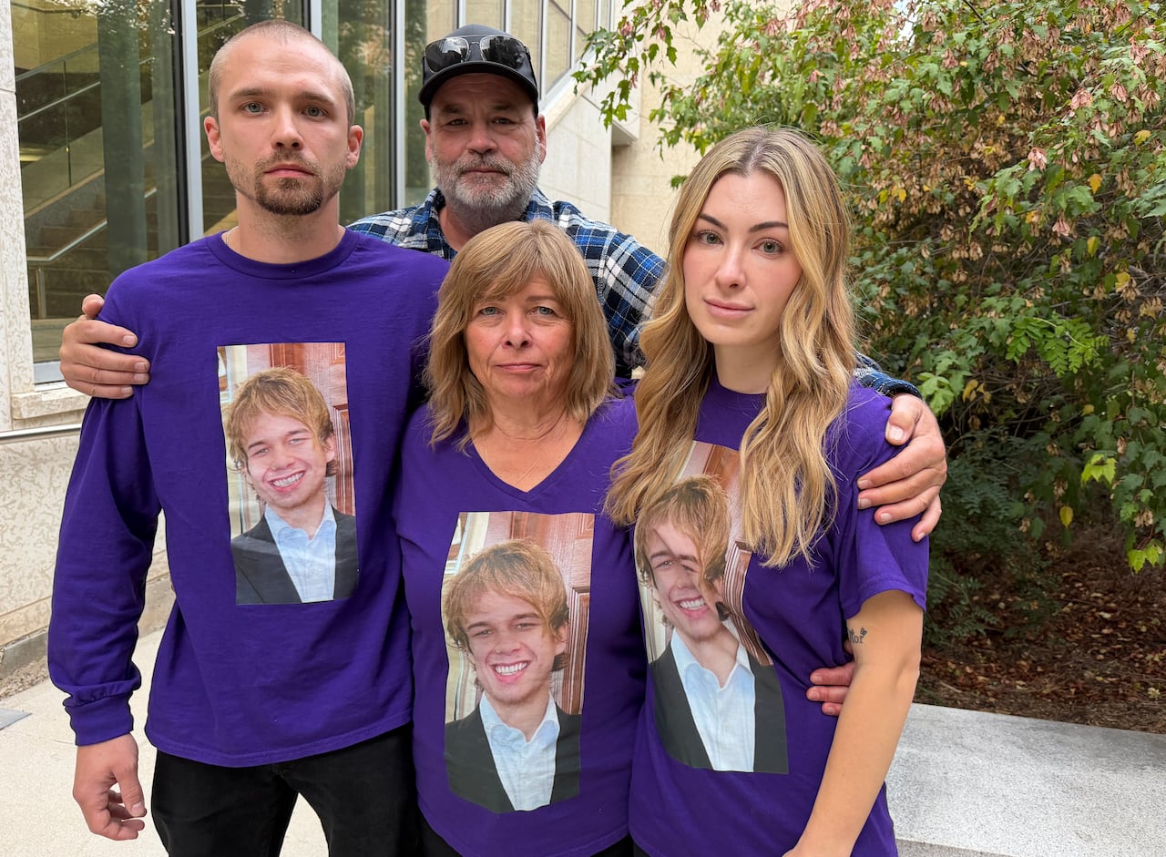 Four people stand, in a big embrace. Three of them have purple shirts with a photo of a young man on it.