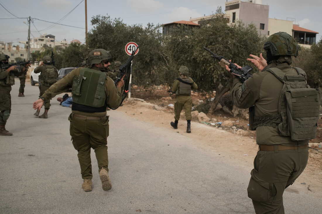 Israeli soldiers move toward a Palestinian man lying wounded on a road after they shot him following a settler attack on Palestinians harvesting olives in the West Bank village of Abu Falah, Friday.
