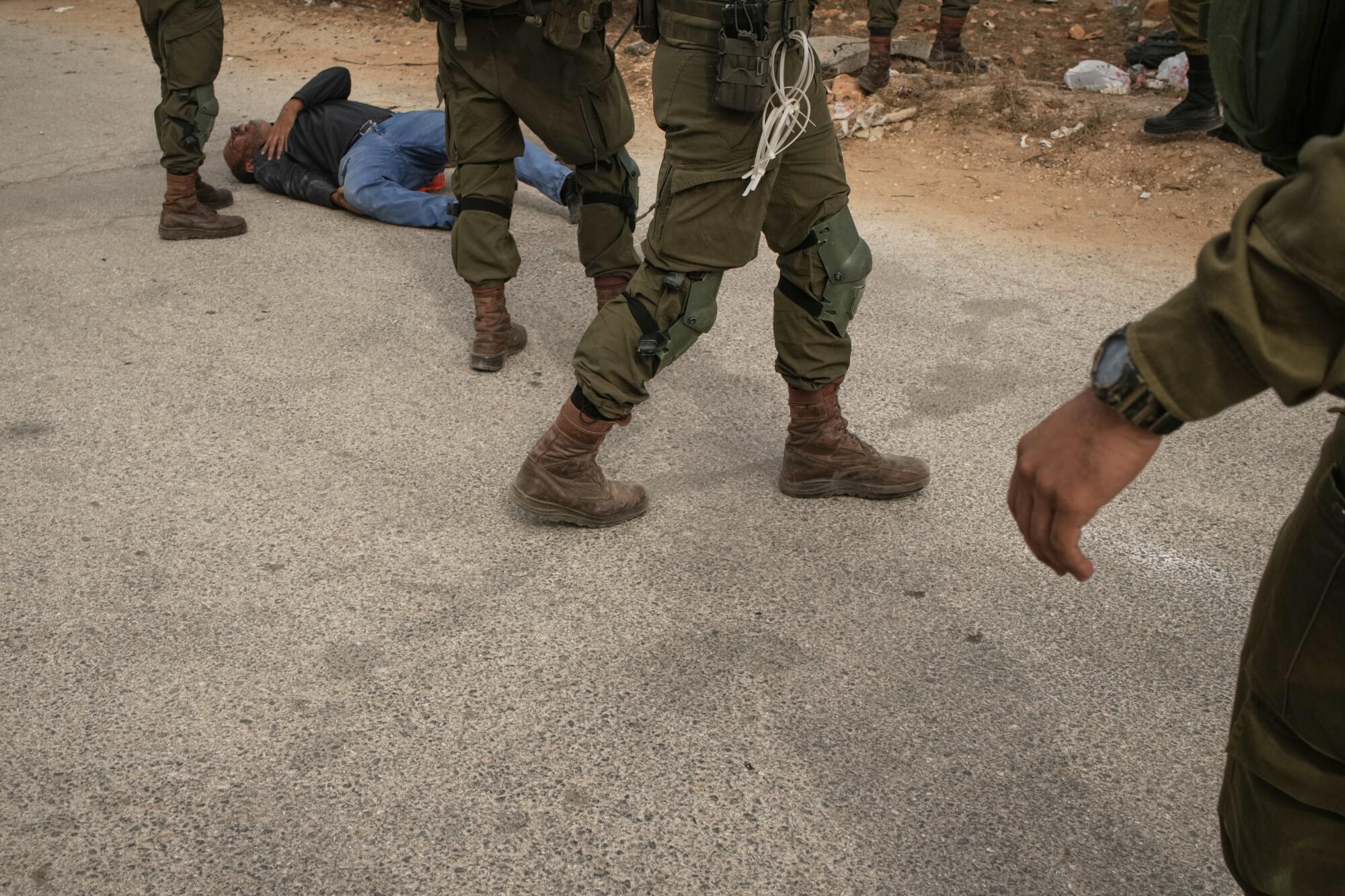 Israeli soldiers stand beside a wounded Palestinian man lying on a road