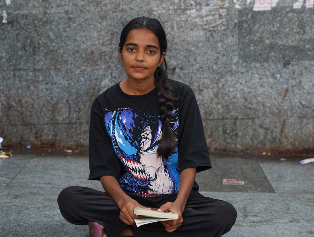 Shalini Yadav, 20, holds a copy of the book “The God of Sins” as she sits on the pavement.