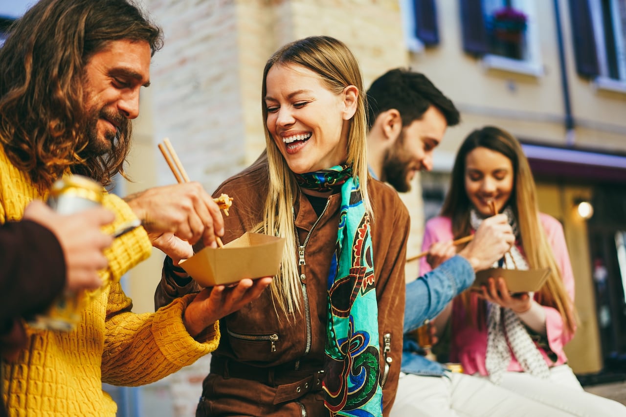 Two men and two women sit outside eating from take-out containers.