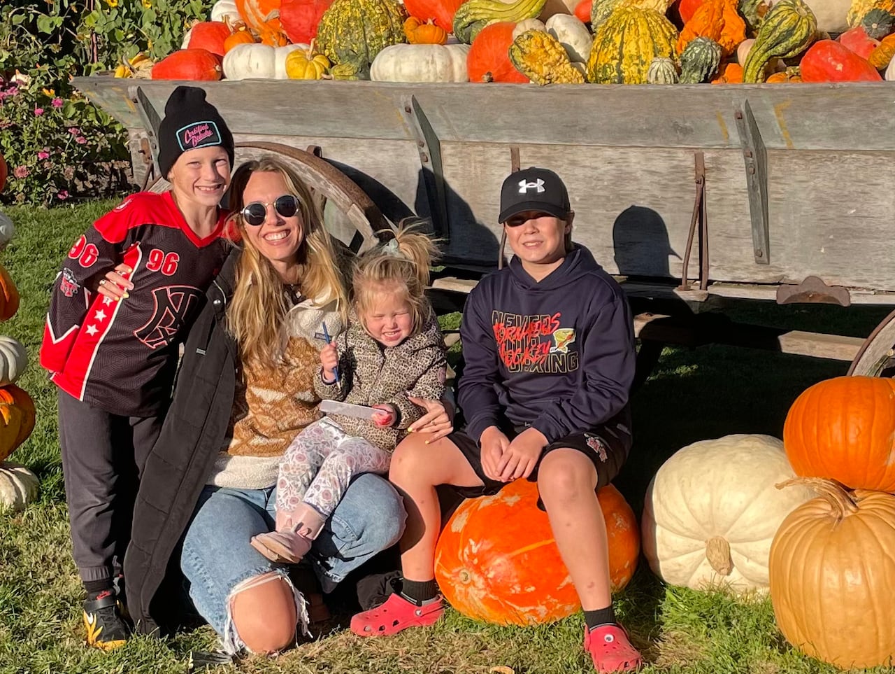 A woman and three children sit next to a wagon full of pumpkins.