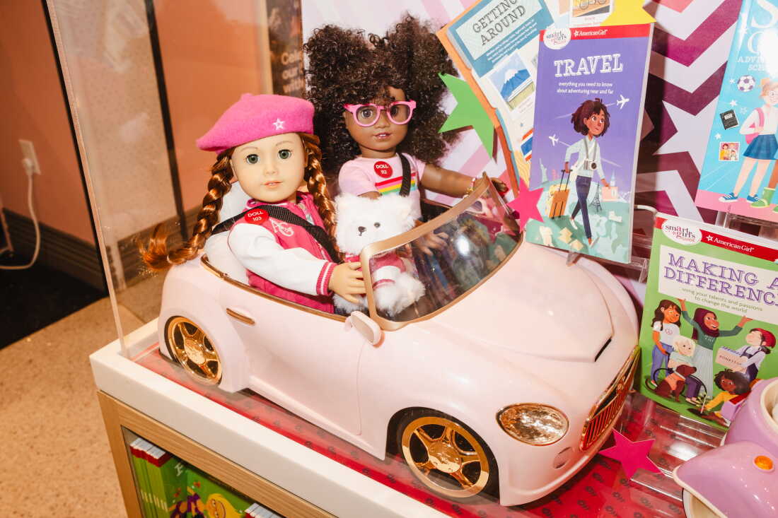 Two dolls and a small white dog are displayed inside a pink car at the American Girl store.