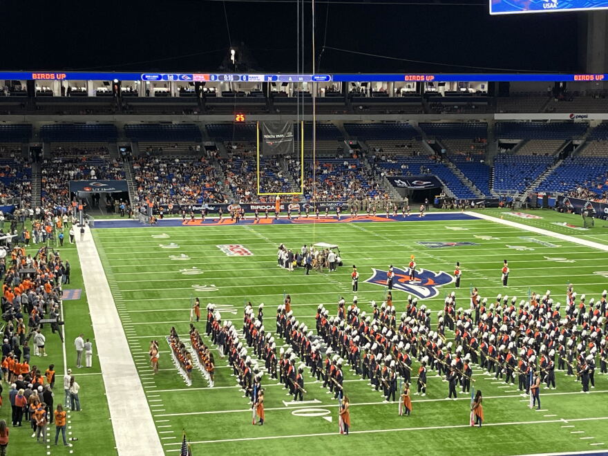 A group of medical personnel and others gathers around a person on the field at the Alamodome on Saturday, Oct. 17, 2026, after a military service member fell while rappelling from the stadium's rafters ahead of the UTSA-Navy football game.
