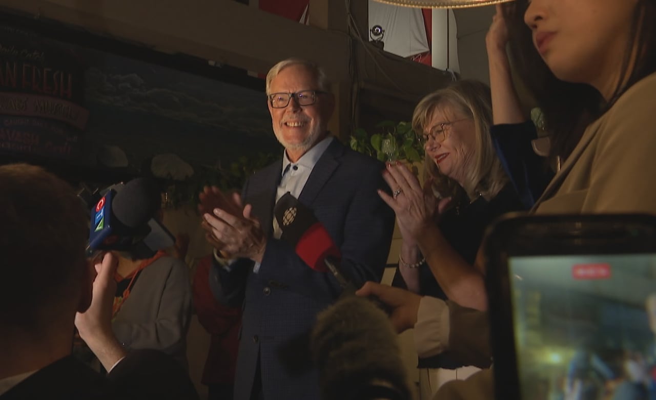 A man in a blue suit speaks to a crowd of enthusiastic supporters.