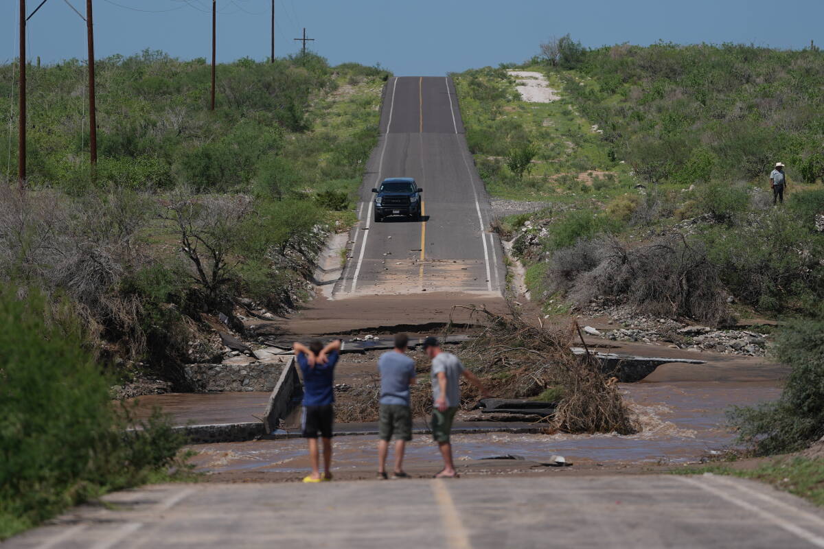 Men survey a road damaged by a swollen river along the road to Las Barrancas