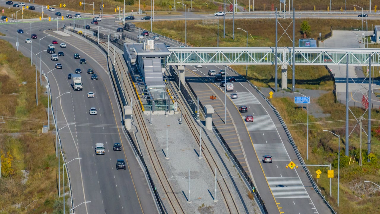 A light rail station in the middle of a highway in early autumn.