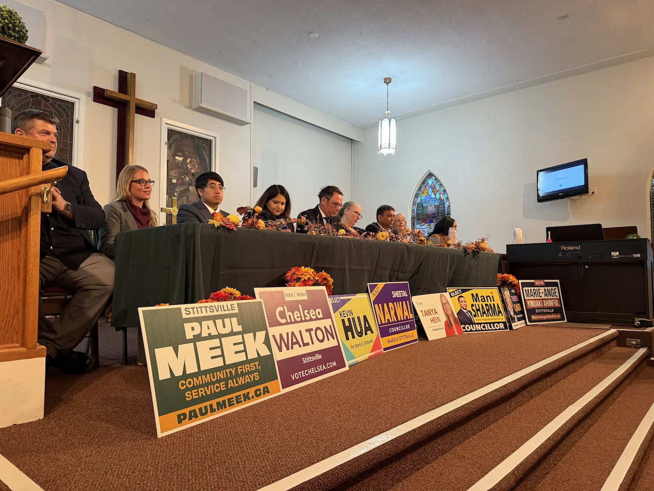 A group of nine people sit in a row behind campaign signs.