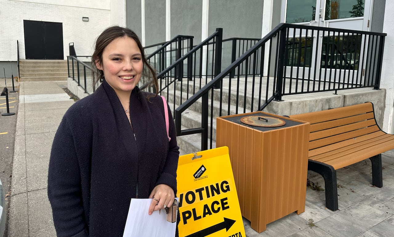 A woman stands near a sign that says "Voting Place."
