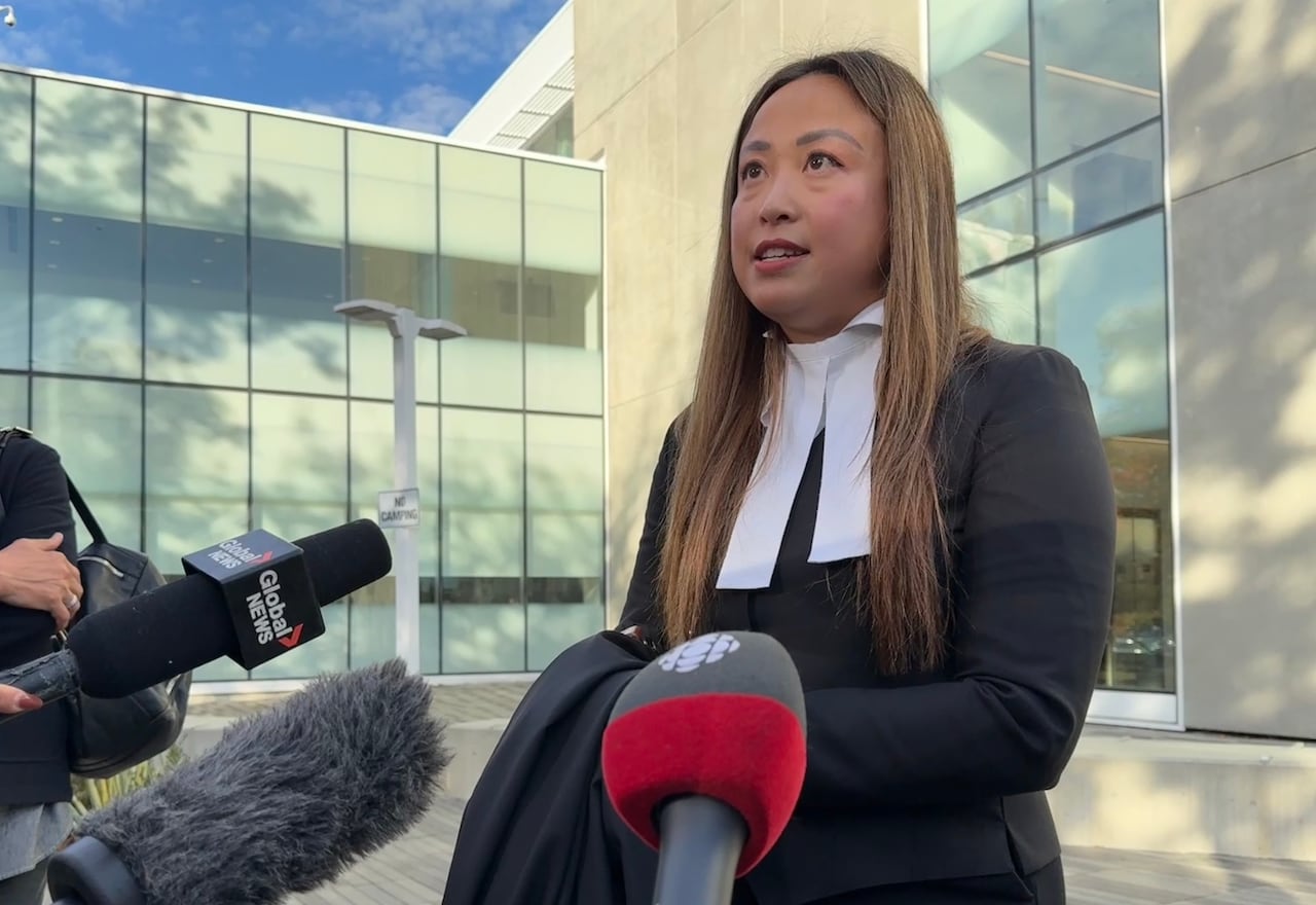 a woman in black lawyers robes speaks in front of news media microphones
