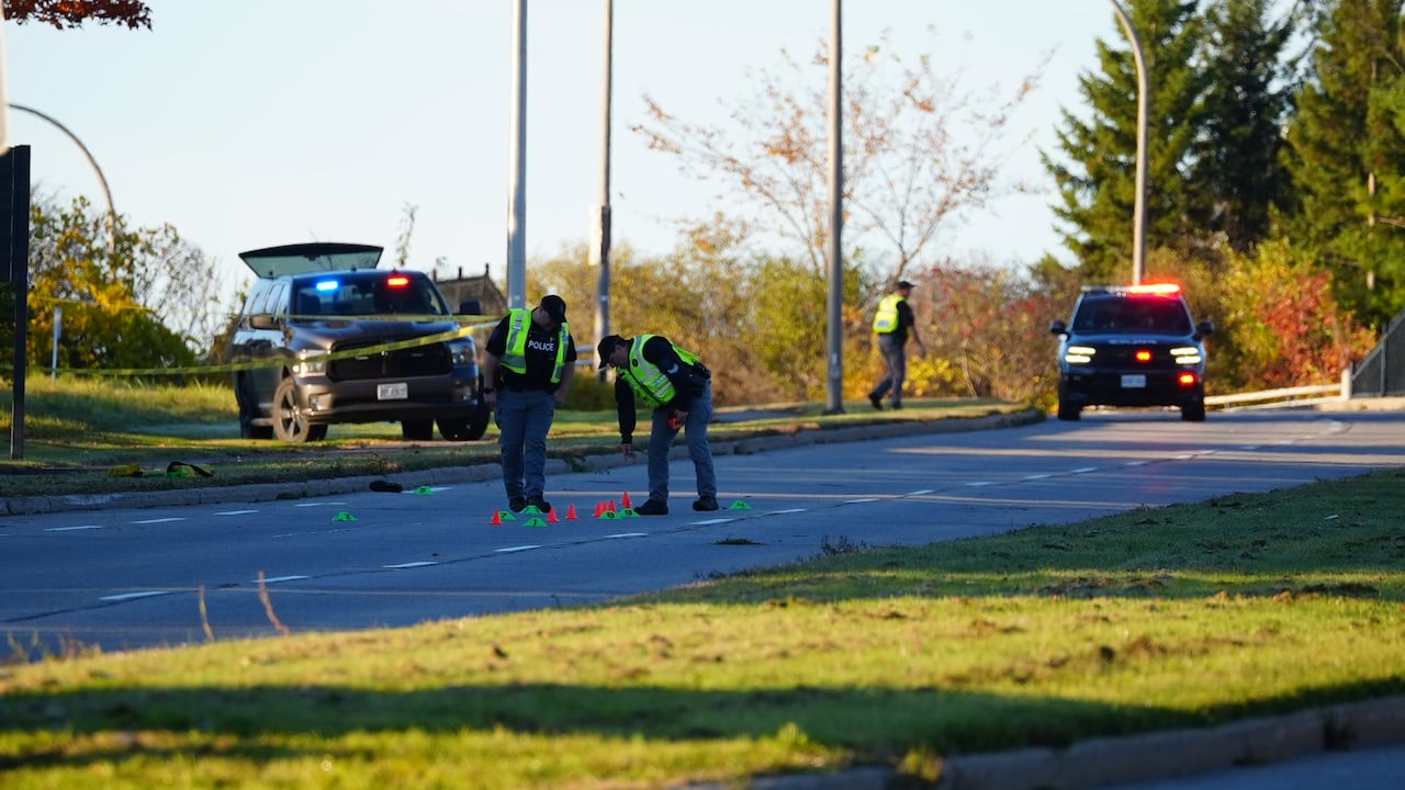 Two crash investigators lay down multicoloured cones on a road after a crash. It's a sunny summer morning.