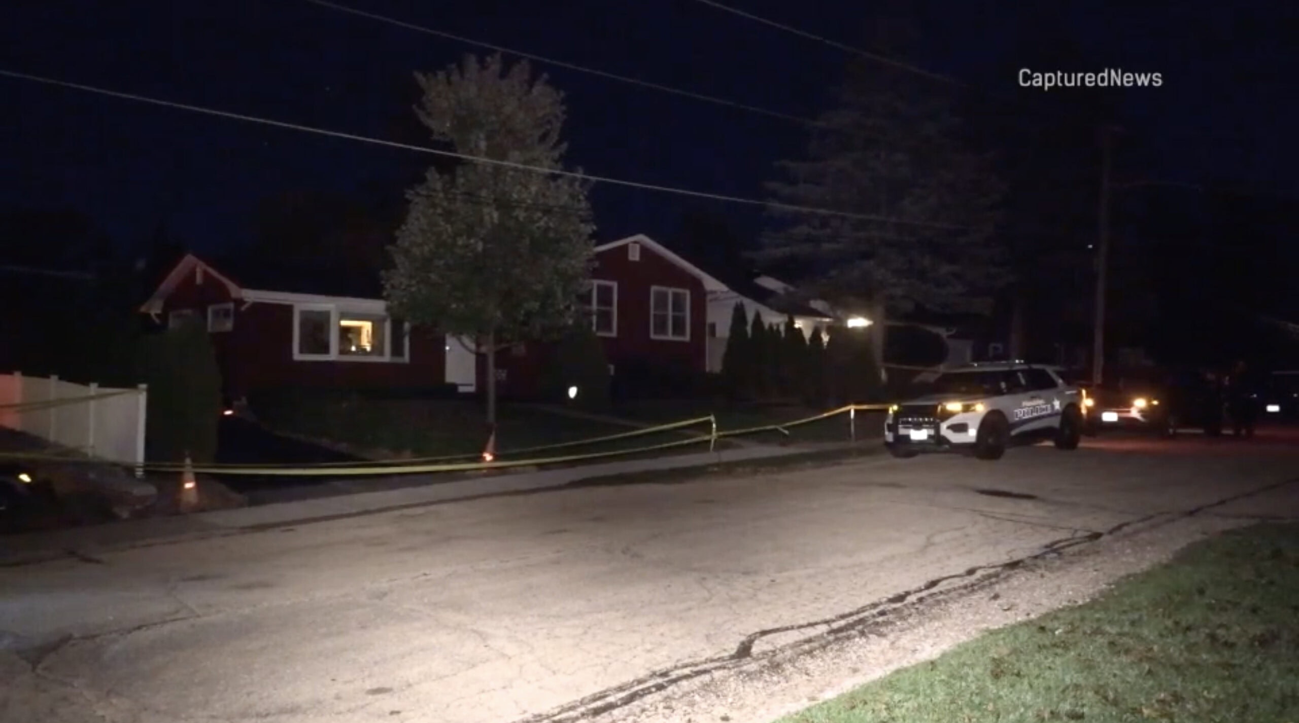 Crime scene tape stretches along a residential street at night with a police squad car parked nearby