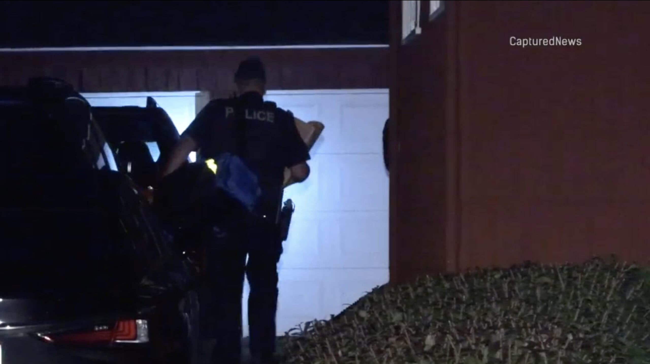 A police officer carries items past a vehicle outside a home at night