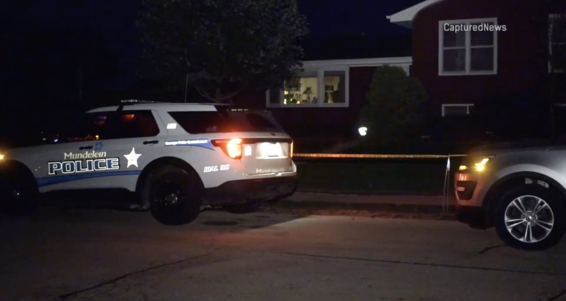A Mundelein police squad car parked outside a home with crime scene tape at night