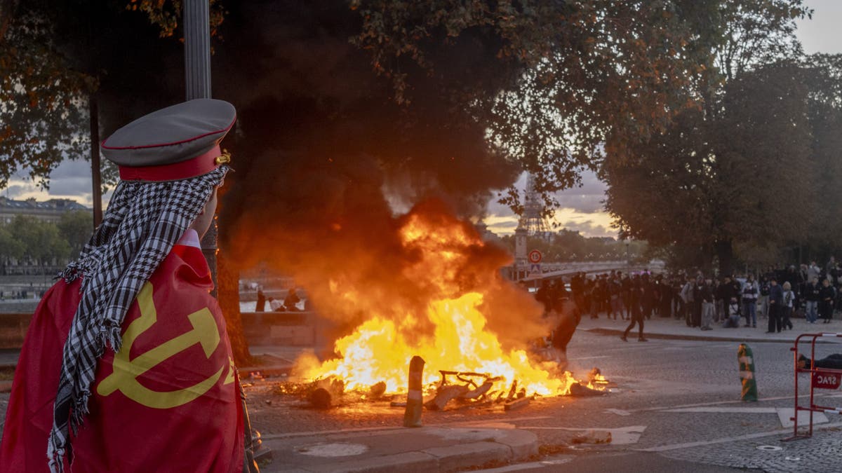 A protester watches a fire burn at a demonstration in Paris, France, on Saturday, Oct. 17, 2026. Rioters attacked French public buildings and looted stores in cities including Paris as protests against the high cost of living drew more than half a million people, underscoring the nation's challenges ahead of presidential elections next year. Photographer: Nathan Laine/Bloomberg via Getty Images