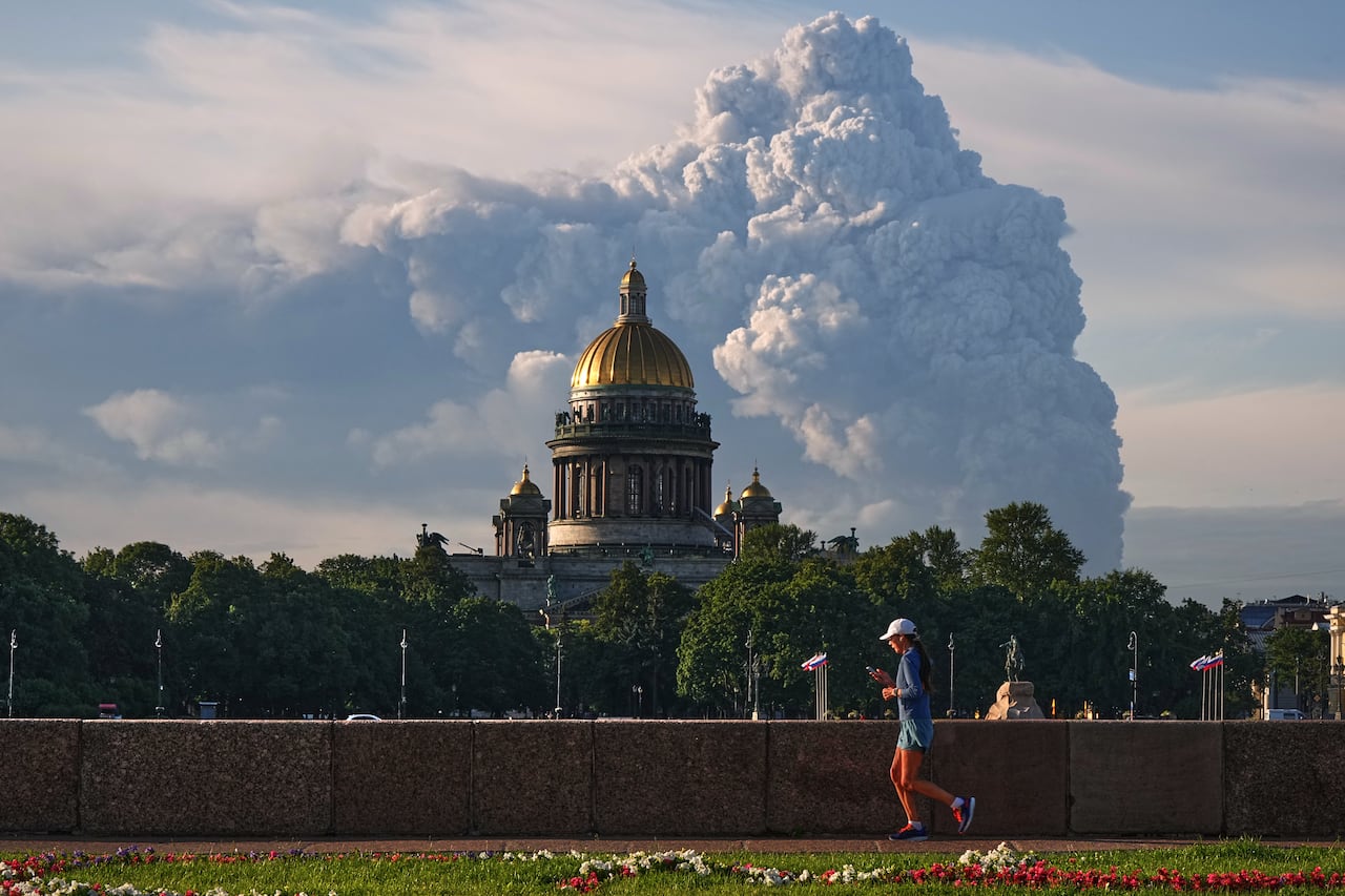Smoke from drone strike in St. Petersburg rises behind St. Isaac's Cathedral as a jogger runs across the foreground of the image.