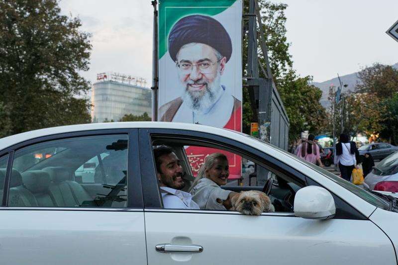 A man and a woman ride in a car with a dog past a portrait of Iran's Supreme Leader Mojtaba Khamenei in Tehran, Iran, Wednesday, Oct. 21, 2026. (AP Photo/Vahid Salemi)